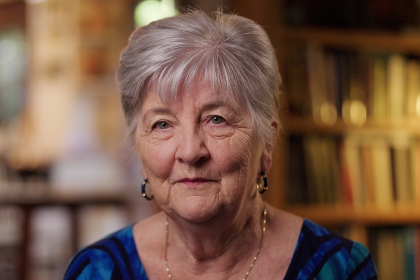 Grey haired woman sits in living room with bookshelves behind her