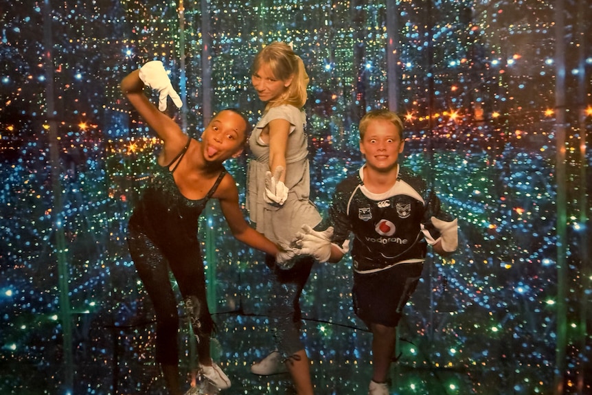 Three children posing for the camera in a light-filled sensory room at a theme park.
