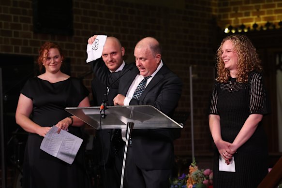 Jenny Piper’s husband Bruce holds up the family crest she designed on a hankie.