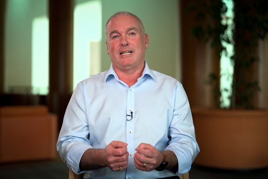 A man wearing a pale blue business shirt holds his hands in front of him