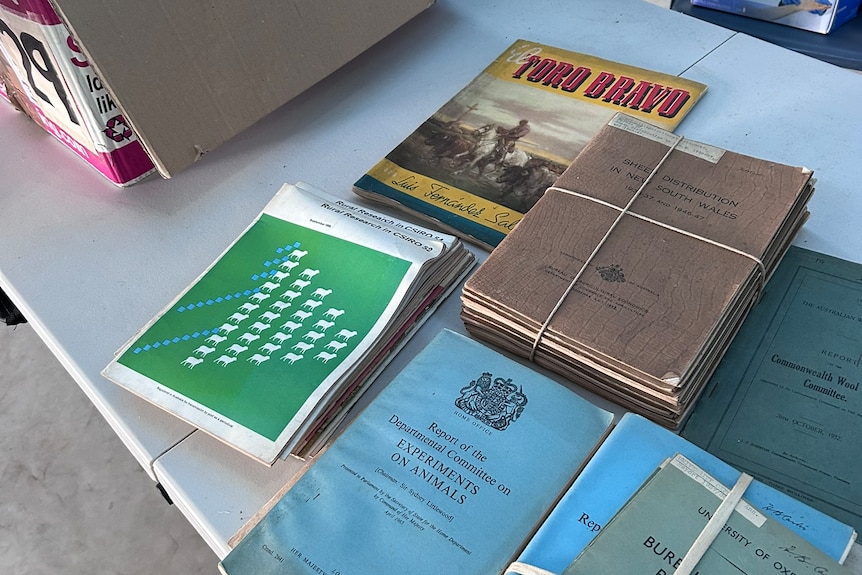 Books and old papers in bundles on a table, some of them are official Australian government documents, others are textbooks.
