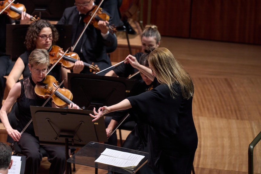Simone Young leading the string section on a performance of Beethoven's Ninth, her arms outstretched.