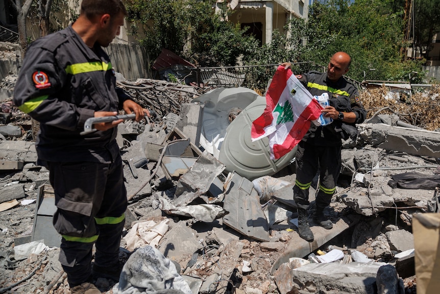 A uniformed officer holding up a Lebanese flag while standing with another worker in a pile of rubble.