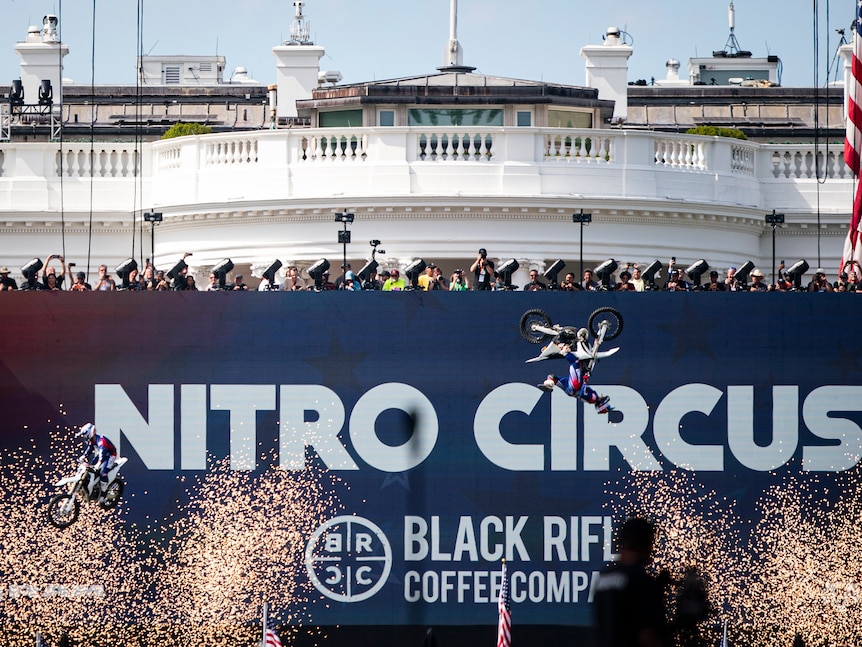 A motorbike flips in the air in front of a giant banner, which covers up the White House in the background.
