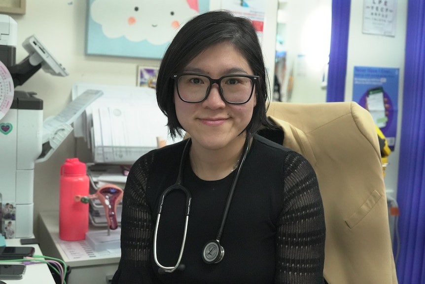 A woman with a stethoscope around her neck smiles.