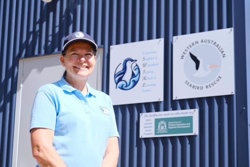 A woman smiles wearing a cap and standing in front of a shed with a sign reading Western Australia seabird rescue.