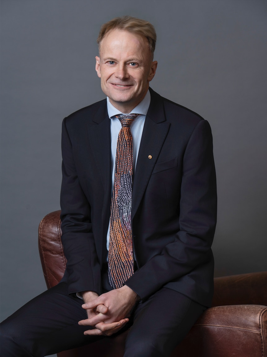 Richard Scolyer in suit seated with hands clasped in front of him, smiling