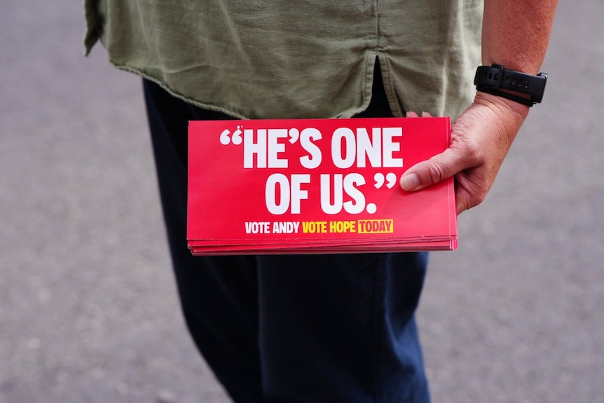 A woman's hand holding a stack of papers which say He's One of Us on them.