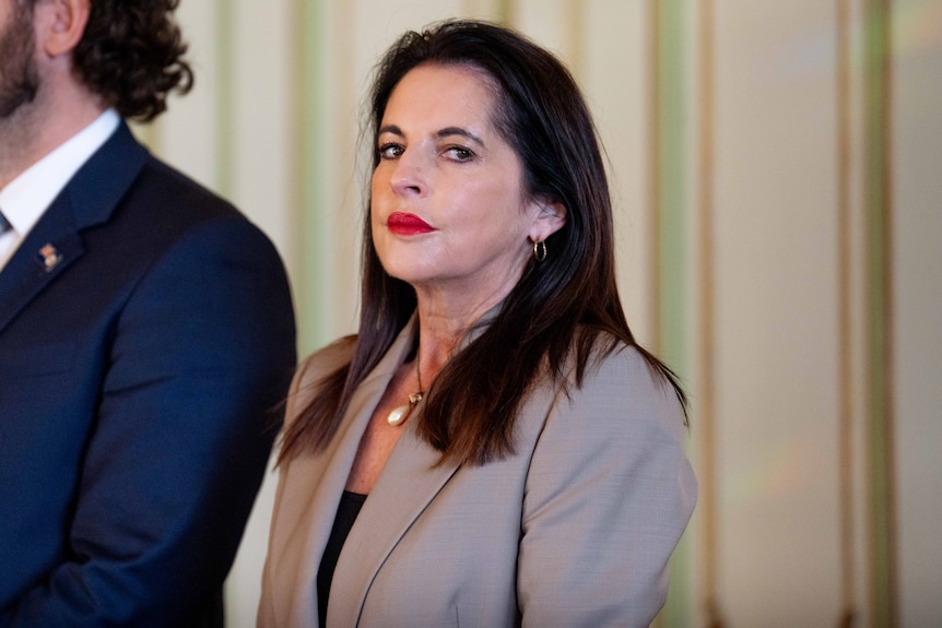 A woman dressed formally looks to the distance, next to men in suits