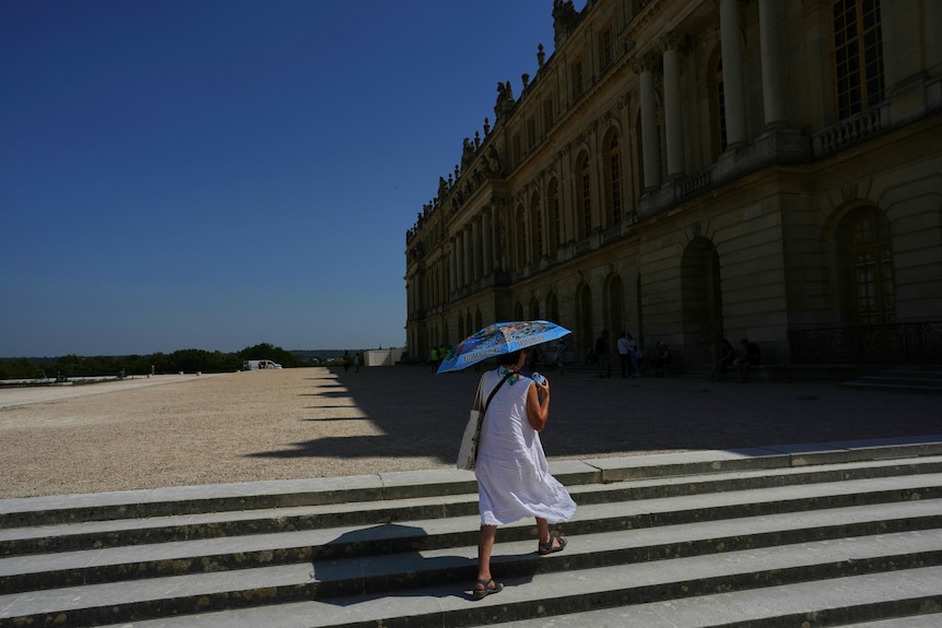 A woman shields herself from the sun with an umbrella as she walks in the garden of the Palace of Versailles.