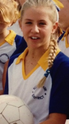 Stacey Marinkovich holds a netball while posing for a photo in a yellow and blue netball outfit.