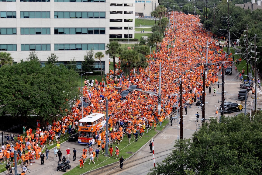 an aerial view of a large parade of people wearing orange and double decker orange bus 