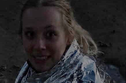 A woman wrapped in foil seated on a beach in the dark