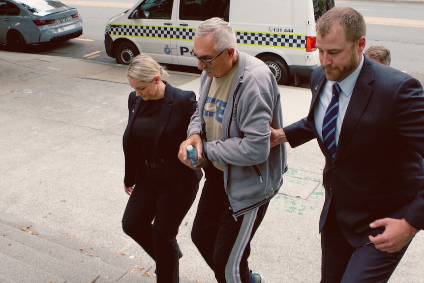 A handcuffed man escorted from a house by two AFP officers.