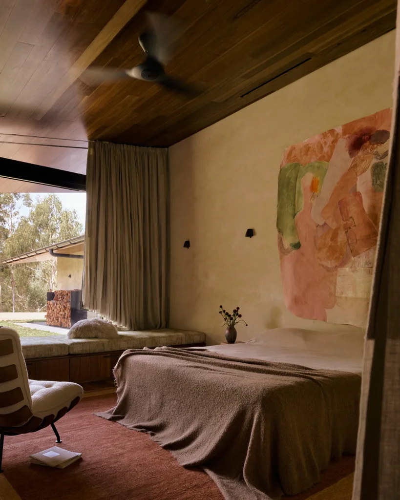 A modern bedroom with an abstract artwork, minimal furniture and windows framing greenery views