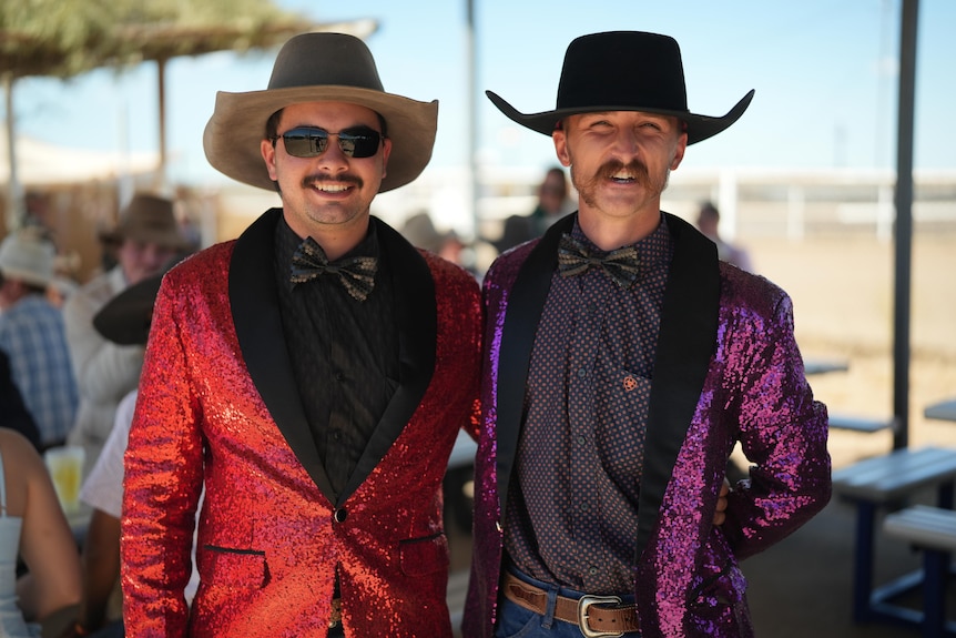 Two men in cowboy hats and sparkly suits smile