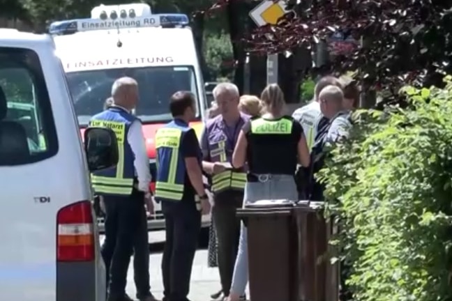 Police stand around wearing hi-vis jackets, talking to journalists and citizens.