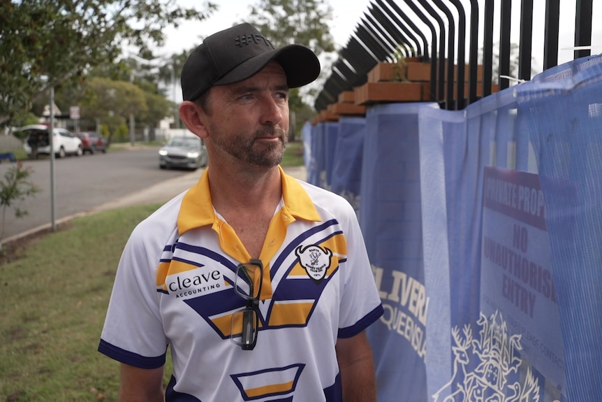 A man in a cap and jersey standing next to construction fence.
