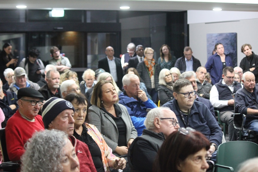 A crowd of people at a public meeting in a community hall.