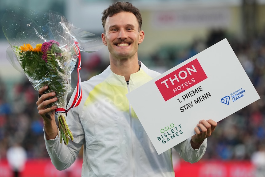 Kurtis Marschall smiles and holds flowers and a large white card.