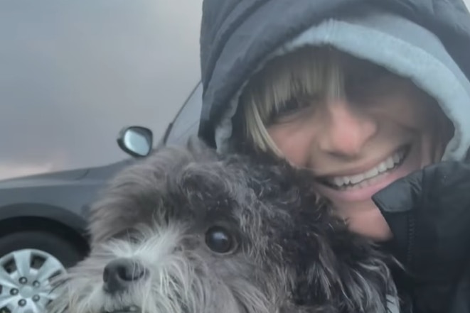 A woman in a raincoat cuddling her dog.