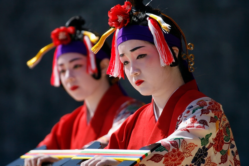 Dancers in pale makeup wearing colourful dress.
