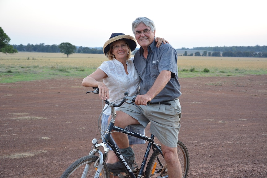 A male and female couple smiling in front of a black bike.