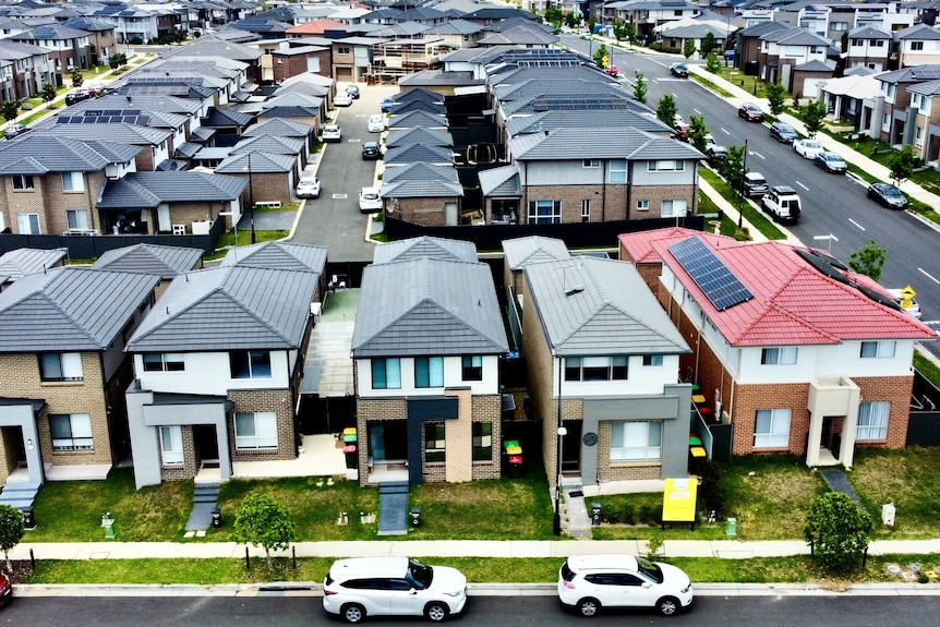 Aerial shot of dozens of houses in neat rows in a new outer-suburban housing estate.