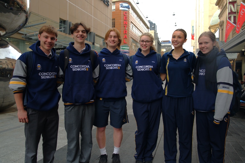 Six teenagers stand in a line: three male and three female.