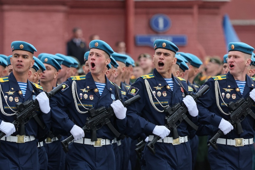 Many men in military uniforms march with weapons.