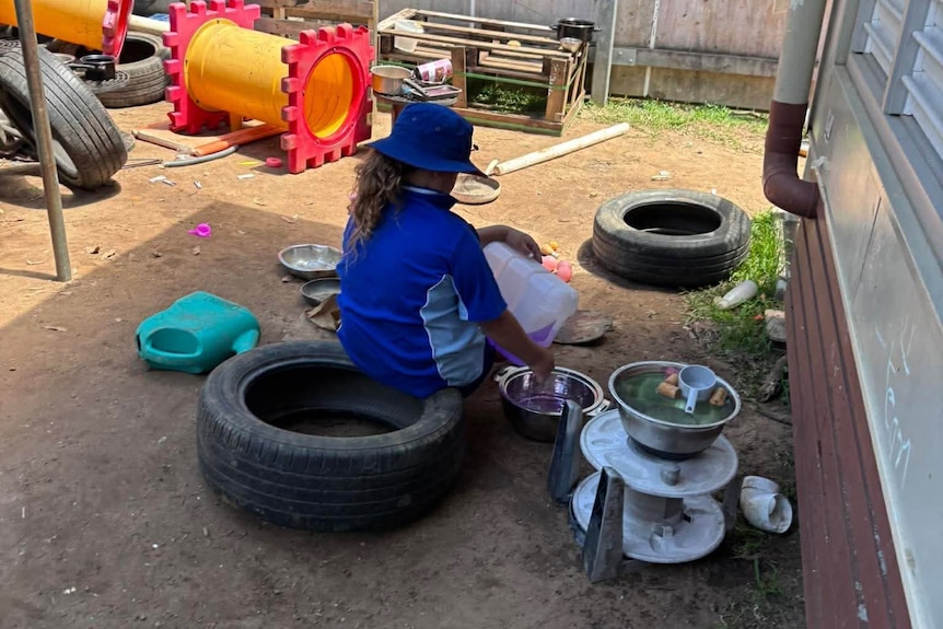 a child sits on a tyre and pours coloured water into a plan