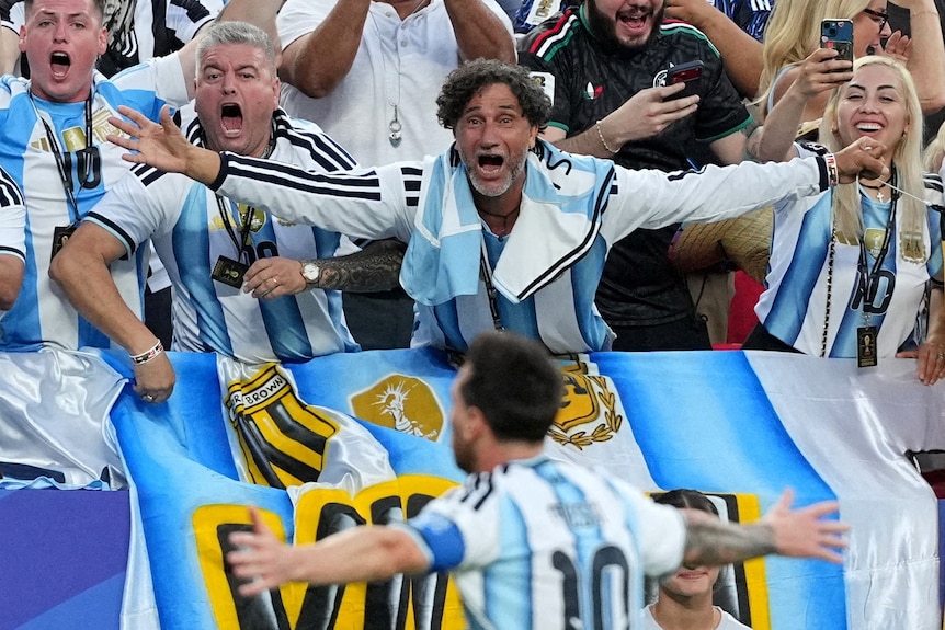 a man in an argentinian jersey raises his hands out to messi