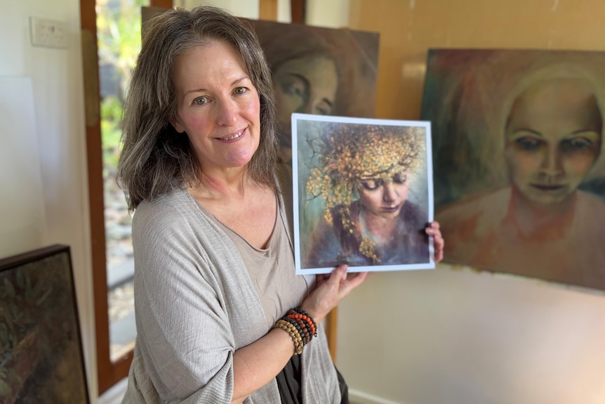 A woman sitting holding a painting in a garden art studio.