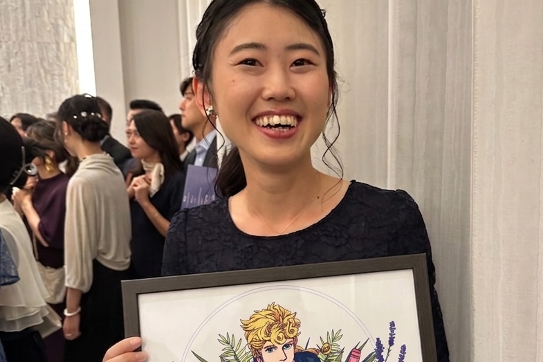 A young woman smiles while holding a picture of an anime character.