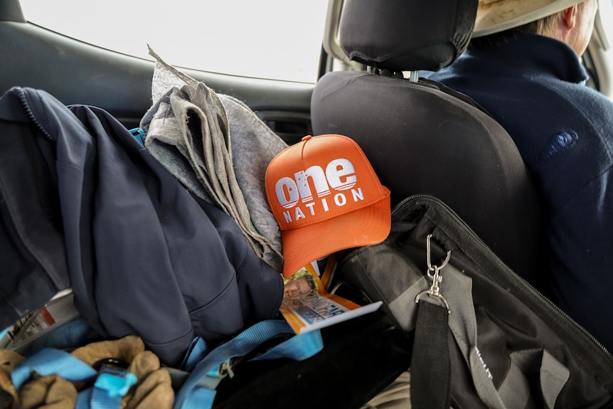 An orange One Nation cap sits amid a pile of belongings in the backseat of a moving ute