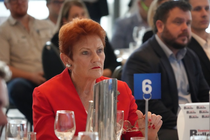 A woman sits at a table in the crowd of a function.