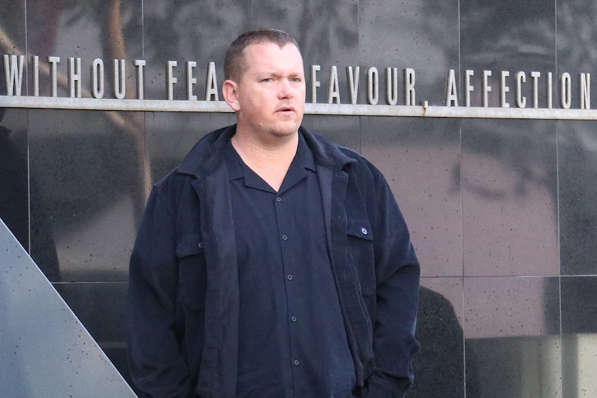 A middle-aged man with short hair, a dark blue shirt and blue jacket stands outside court in Perth.