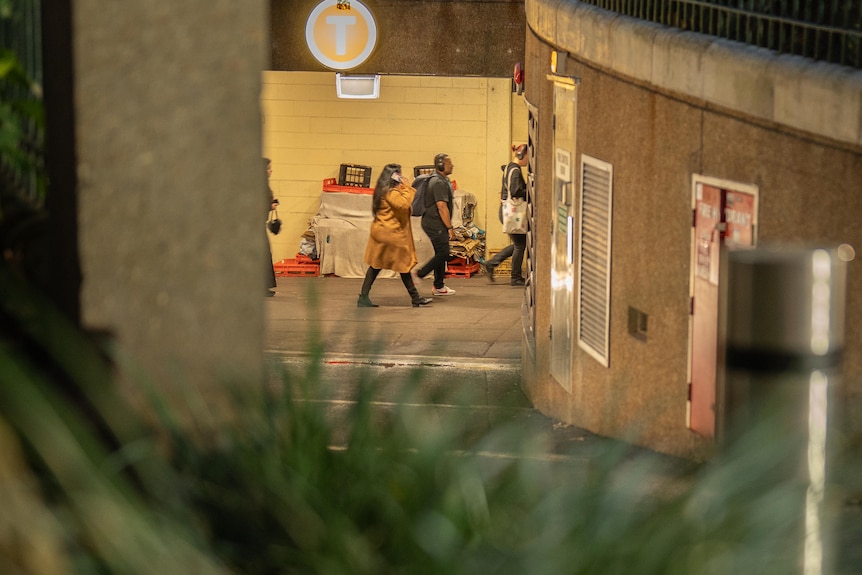 A woman on her phone walks past a homeless person's belongings at St James train station, Sydney.