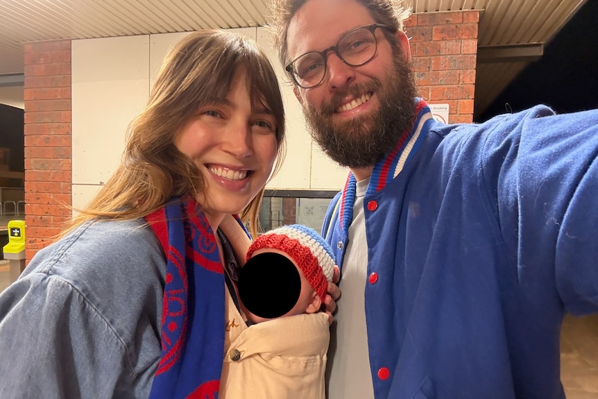 A smiling couple with a small baby in a carrier