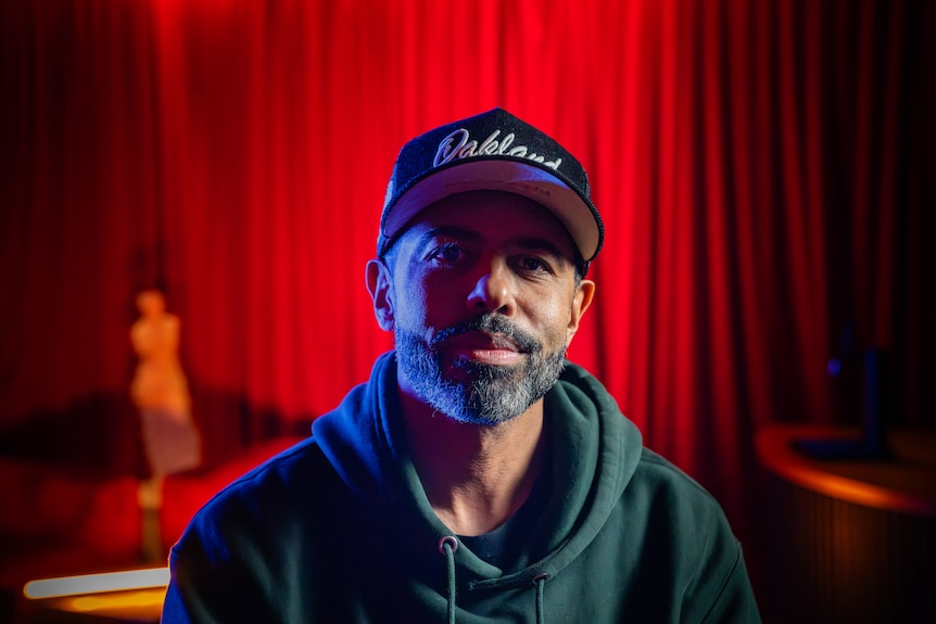 Daveed Diggs sits in front of a red curtain.