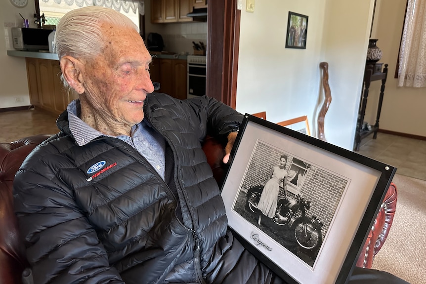 An elderly man looks at a black and white photo of a young woman.