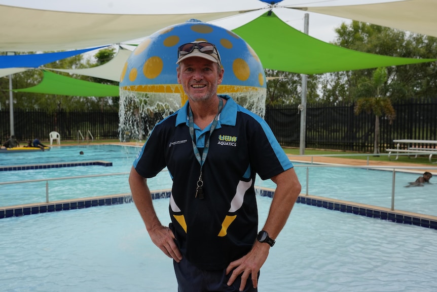 White man in his sixties standing in front of an outdoor pool smiling.