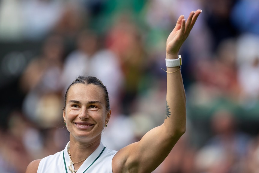 Aryna Sabalenka waves and smiles to the crowd at Wimbledon.