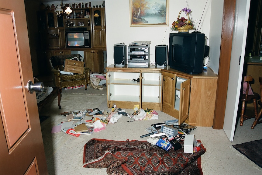 A TV sitting on a wooden entertainment unit with cupboard doors open and objects strewn across the floor.
