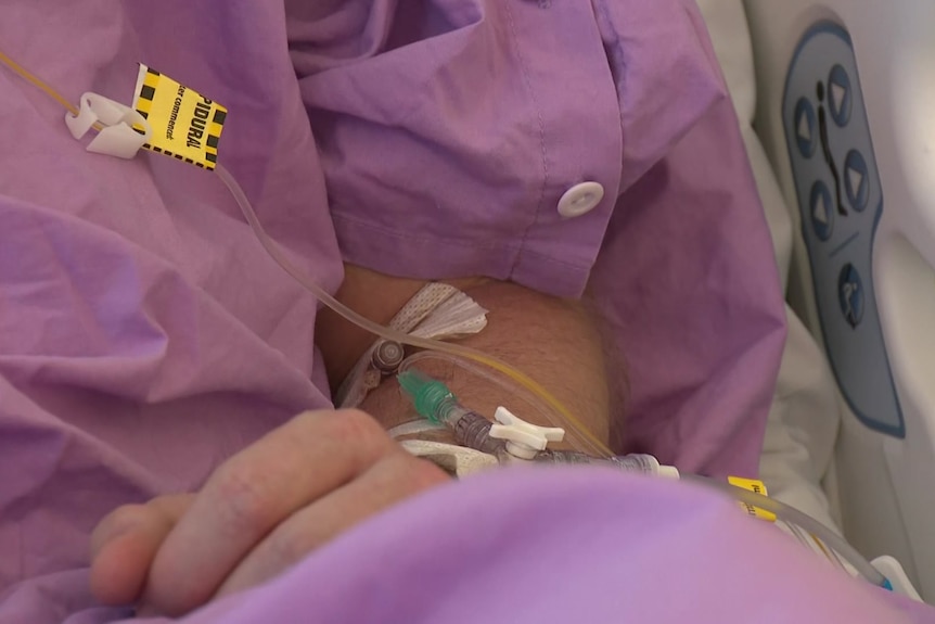A close up of a person in a hospital gown with an IV drip in their arm.