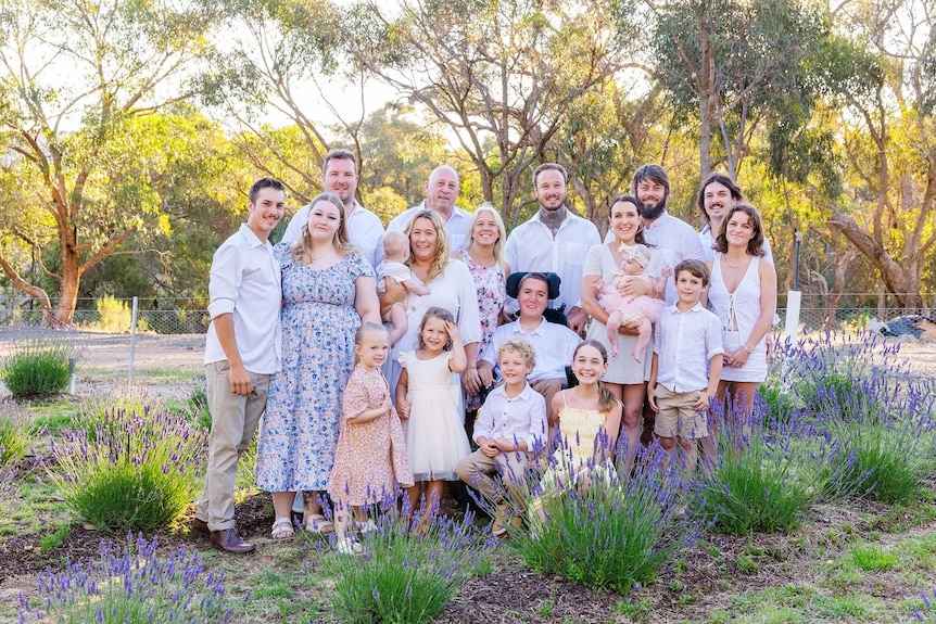 A man in a wheelchair, surrounded by his family in white, yellow and floral clothing, surrounded by lavender