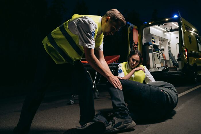 Two paramedics assisting a patient on the ground next to an ambulance at night, showcasing the events nurses encounter.