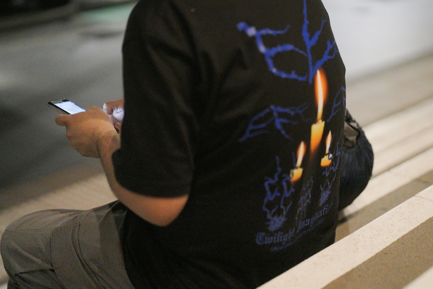 A man sits outide on steps looking at his phone.