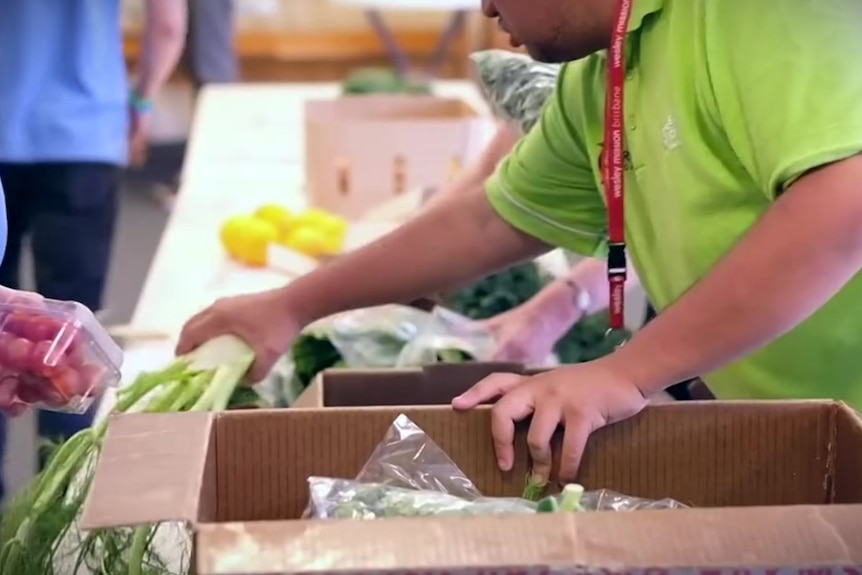 A young man in a green shirt putting fresh vegetables in a box.