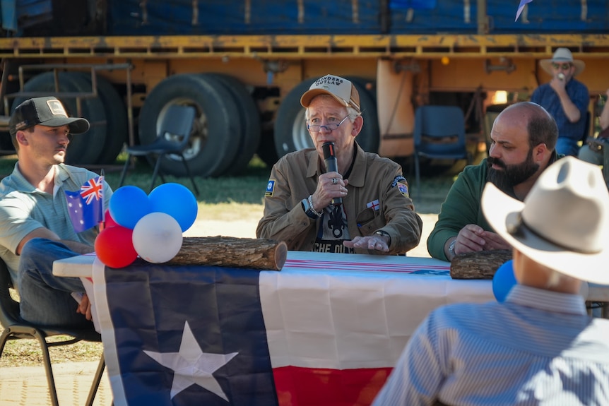 Three men sitting at a desk wrapped in the Texas state flag